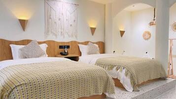 A hotel room with two beds, a wooden headboard, wall-mounted lights, and a macrame wall hanging.
