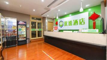 Un espace d’accueil d’hôtel comprenant un comptoir de réception, un réfrigérateur rempli de boissons et un panneau vert orné de caractères chinois.