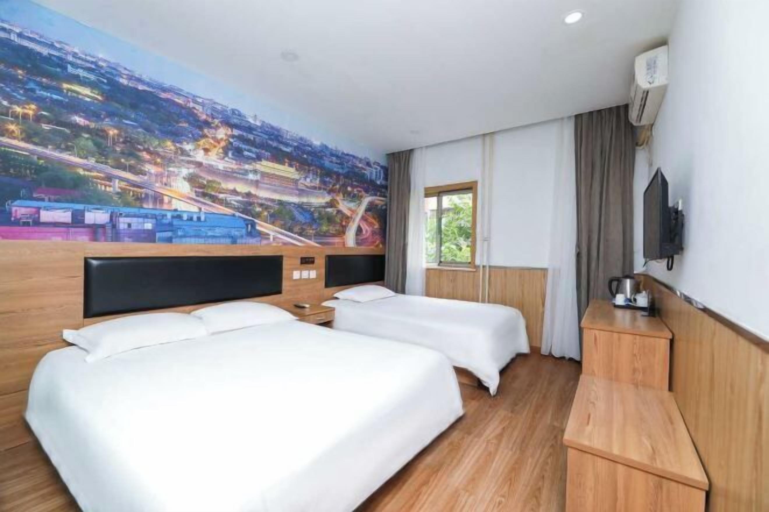 A hotel room with two beds, a large mural of a cityscape, a television, and a window with curtains.