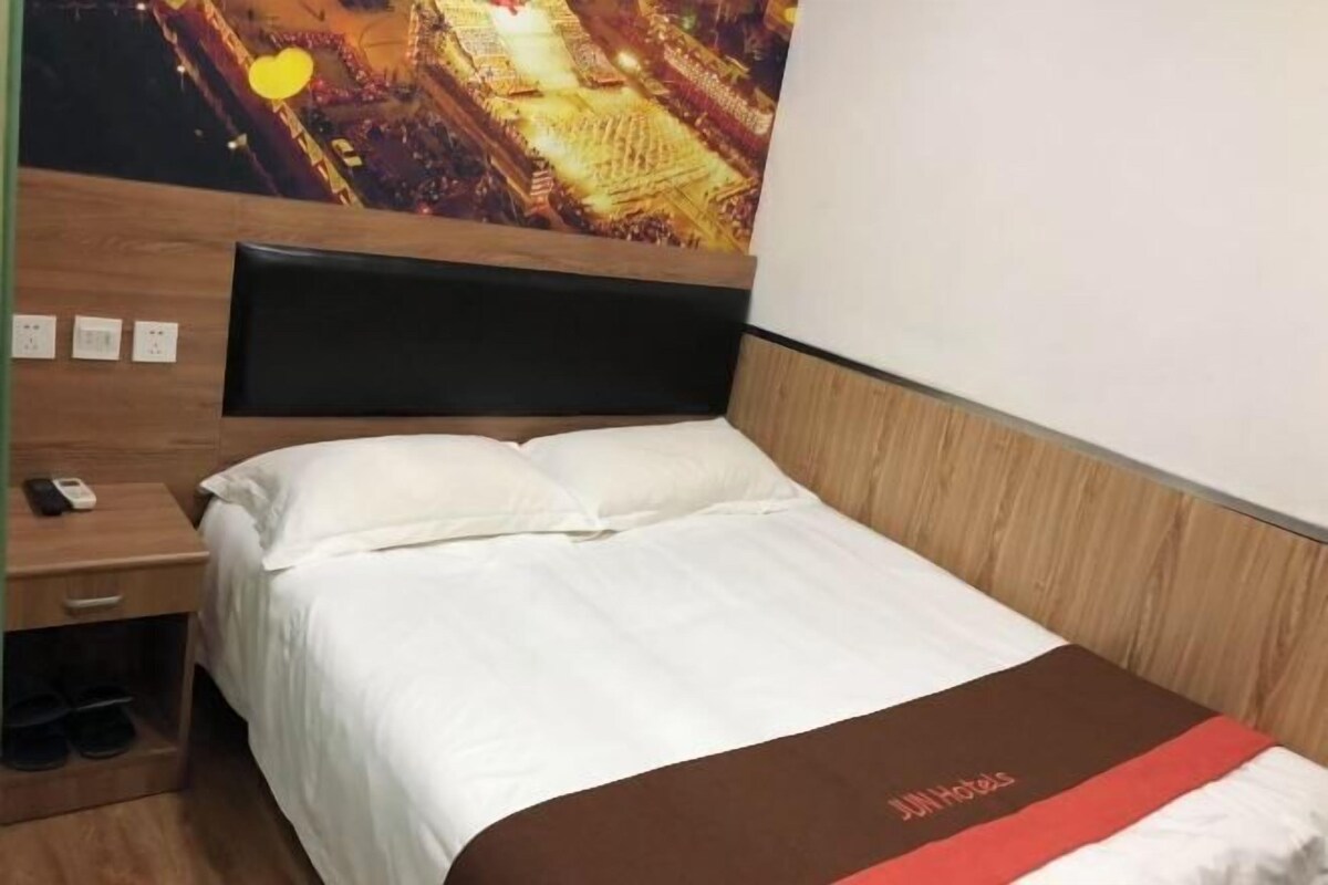 A hotel room with a bed, a nightstand, a wooden headboard, and a wall-mounted TV.