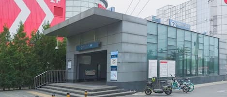 A modern building with a glass facade, a covered entrance, and a red and white sign in the background.