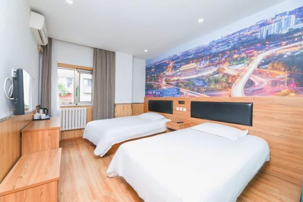 Habitación de hotel con dos camas, suelo de madera, un ventanal grande, un radiador, un televisor y un mural con vista a la ciudad.