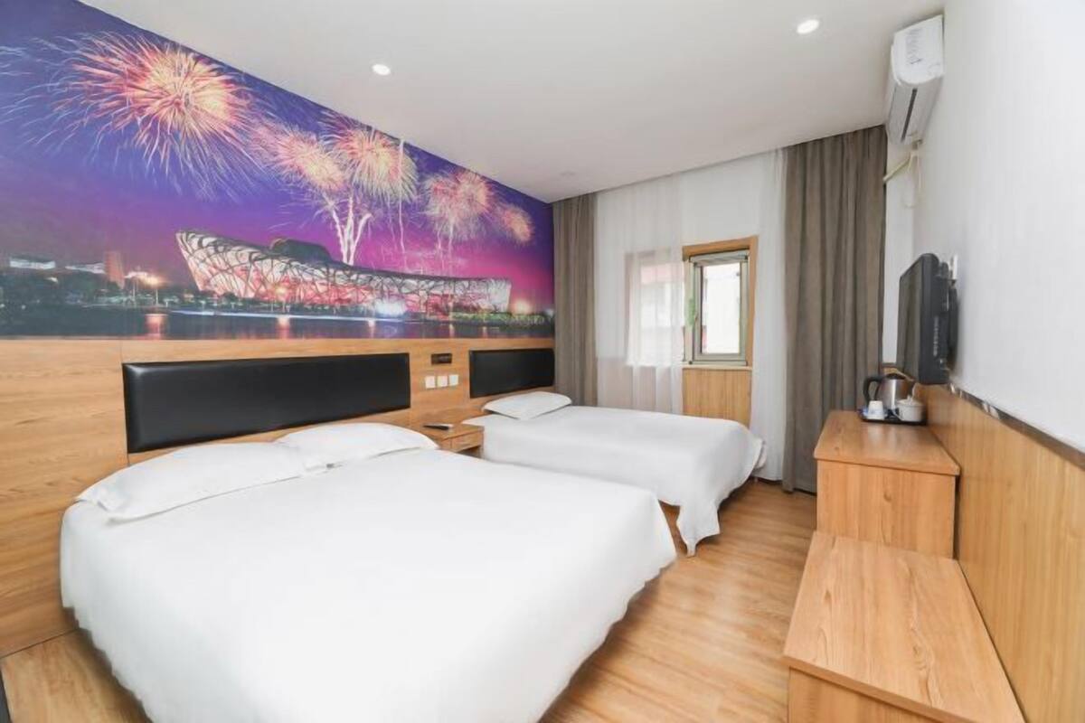 Una habitación de hotel con dos camas, un cabecero de madera, un televisor de pantalla plana, un escritorio y un mural de fuegos artificiales en la pared.