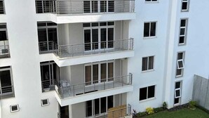 Un edificio residenziale a più piani con balconi, un tetto piano e un piccolo giardino con erba e piante.