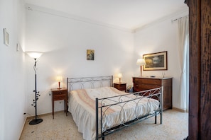 Ein Schlafzimmer mit einem Metallbettgestell, zwei Nachttischen mit Lampen, einer Holzkommode und einem einzelnen Wandbild.