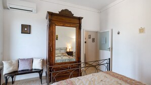 A bedroom with a bed, a wooden wardrobe with a mirror, a bench, and a wall-mounted air conditioner.