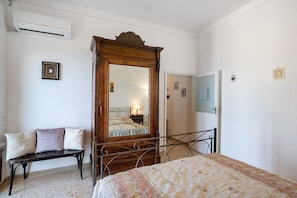 Une chambre à coucher comprenant un lit, une armoire en bois avec un miroir, un banc et un climatiseur fixé au mur.