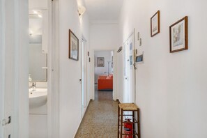 A hallway with white walls, framed pictures, a fire extinguisher, and a visible bathroom with a sink. - Apartment 'Sguardo Sul Golfo' with Sea View, Wi-Fi and Air Conditioning (Massa Lubrense)