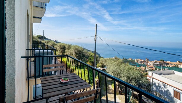 A balcony with a wooden table, a railing, and a view of the sea and town.