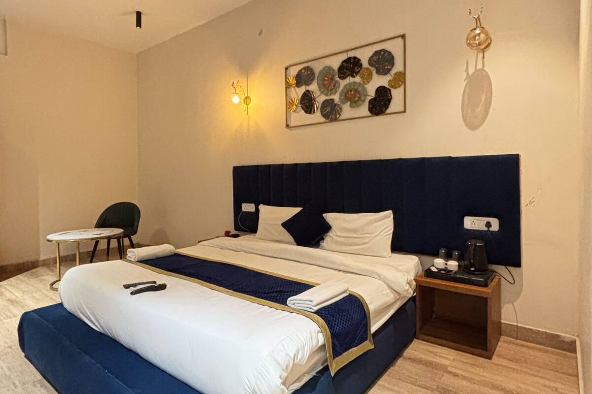 A modern hotel room with a large bed, a bedside table, a chair, and a decorative wall piece.