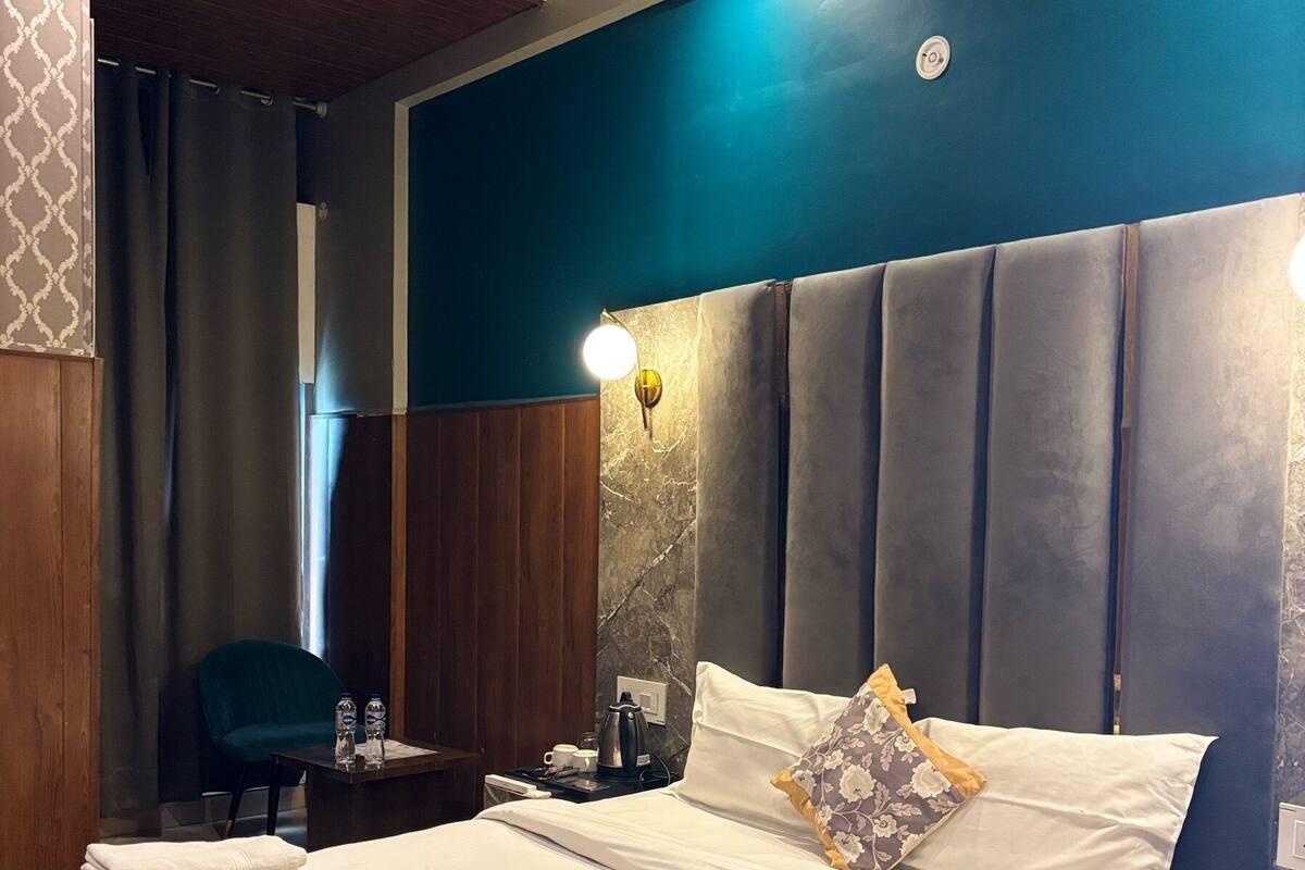 A hotel room with a large bed, a nightstand, a chair, and a desk with a lamp.