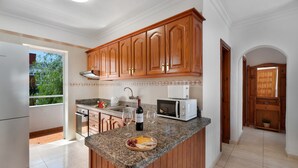 Une cuisine avec des meubles en bois, un four à micro-ondes, une bouteille de vin et un plateau de fromages.