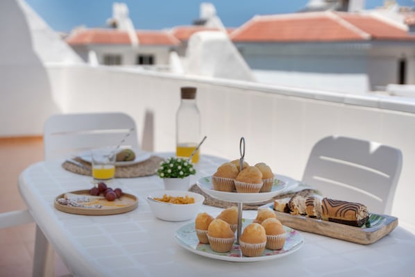 Une table avec des plats et une bouteille, placée sur un balcon avec des bâtiments en arrière-plan.