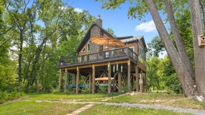 Une cabane avec une cheminée en pierre, une terrasse en bois et un grand parasol.