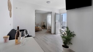 A modern room with a white table, a bottle, two glasses, a potted plant, and a TV mounted on the wall. - Vacation Home 'El Rinconcito De Niña' with Sea View, Private Terrace and Wi-Fi (Tijoco Bajo)