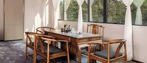 A dining area with a wooden table and chairs, a window with curtains, and a view of trees outside.