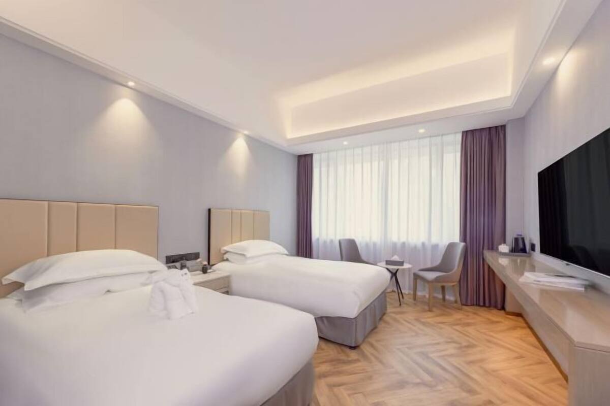 Une chambre d’hôtel avec deux lits, un bureau, une chaise, une télévision et une fenêtre avec des rideaux.