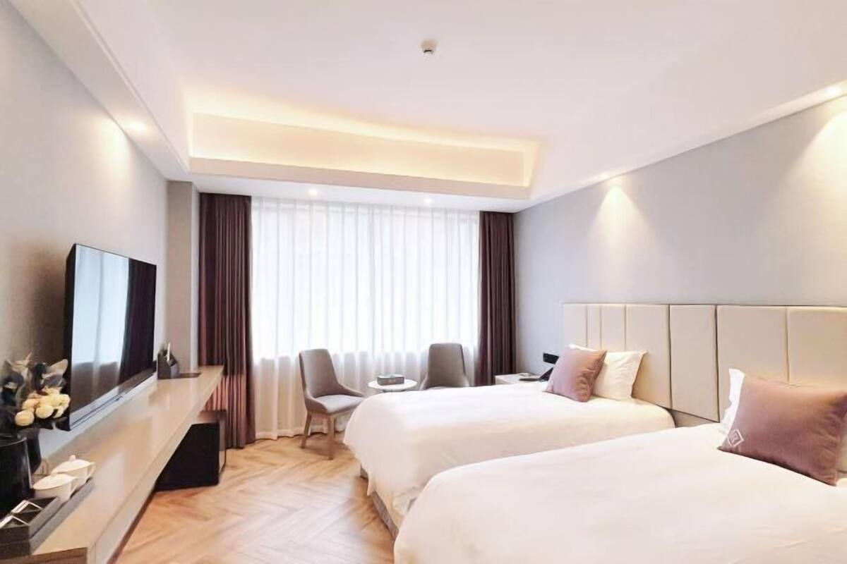 Une chambre d’hôtel avec deux lits, une télévision, un bureau et une fenêtre avec des rideaux.