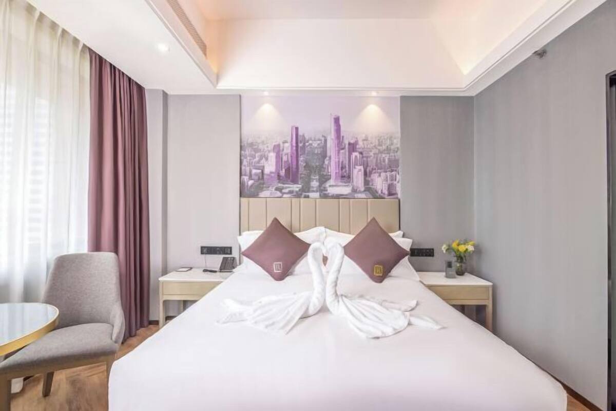 Une chambre d’hôtel avec un lit, une chaise, une table de chevet, une lampe et un tableau représentant un paysage urbain accroché au mur.