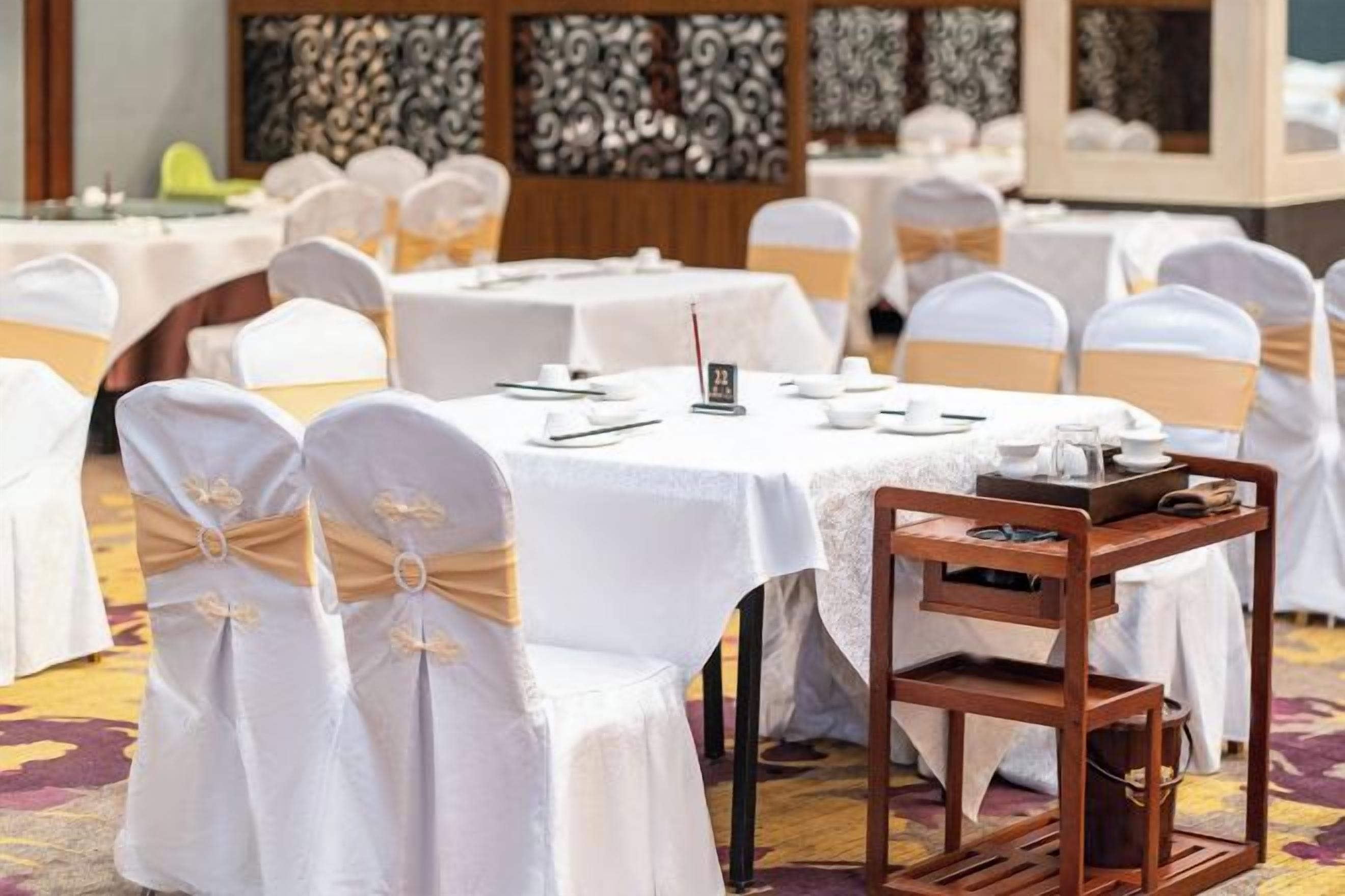 Un salón de banquetes con mesas redondas, manteles blancos y sillas con fundas blancas.