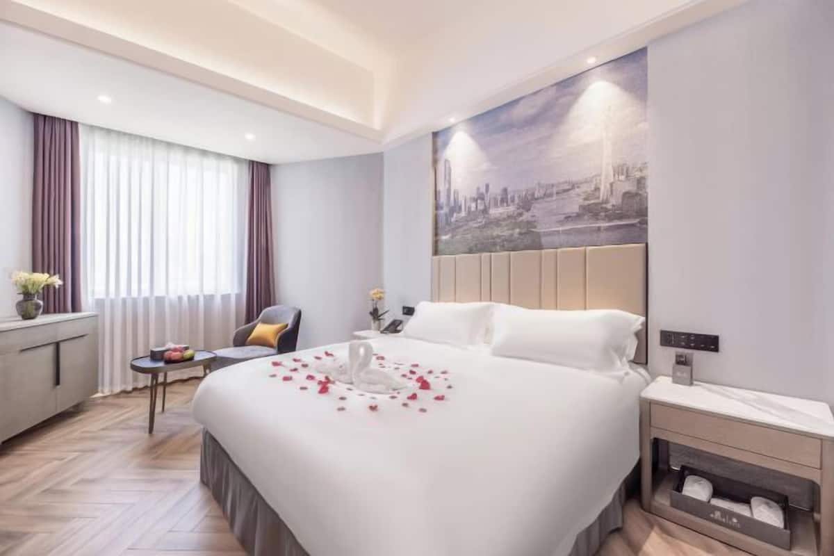 Une chambre d’hôtel avec un lit, une table de chevet, une commode et un tableau représentant un paysage urbain accroché au mur.