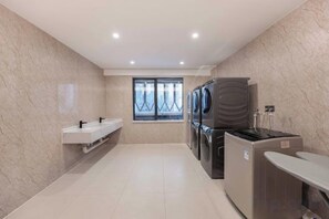 A modern bathroom with a marble wall, a window, a sink, a washing machine, and a toilet. - Tianhe Hotel (Guangzhou)