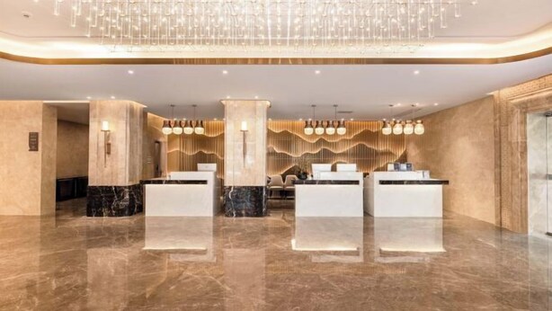 Un vestíbulo moderno con piso de mármol, una recepción central y un elemento decorativo de iluminación.