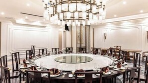 Una mesa redonda de comedor con sillas, una araña y una mesa con superficie de vidrio.