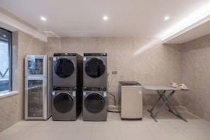 A laundry room with two stacked washing machines, a dryer, and a table with ironing board.