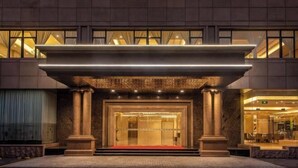 Fachada imponente de un hotel, con amplias columnas y una alfombra roja que conduce a las puertas.