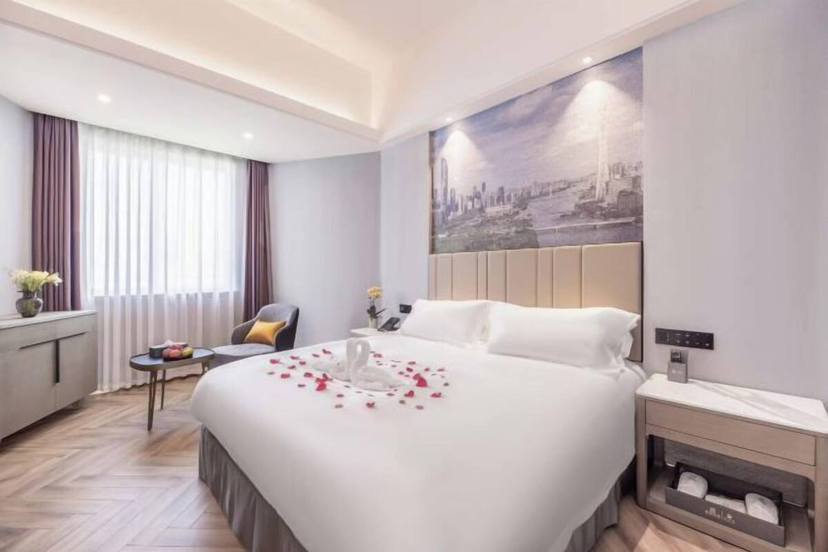 Une chambre d’hôtel avec un lit, une table de chevet, une commode et un tableau représentant un paysage urbain accroché au mur.