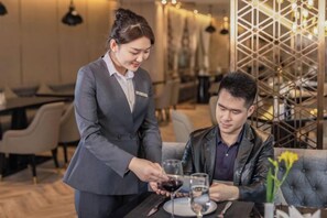 A person serving wine to another seated at a table in a restaurant setting. - Tianhe Hotel (Guangzhou)