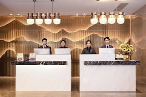 A reception desk with three staff members, laptops, and a vase of flowers. - Tianhe Hotel (Guangzhou)