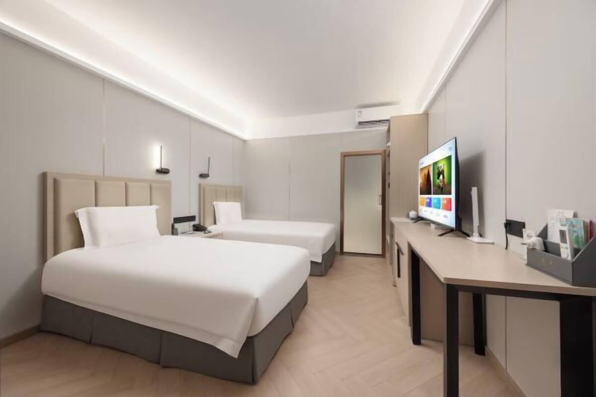 Une chambre d’hôtel avec deux lits, un bureau, une télévision et une porte.