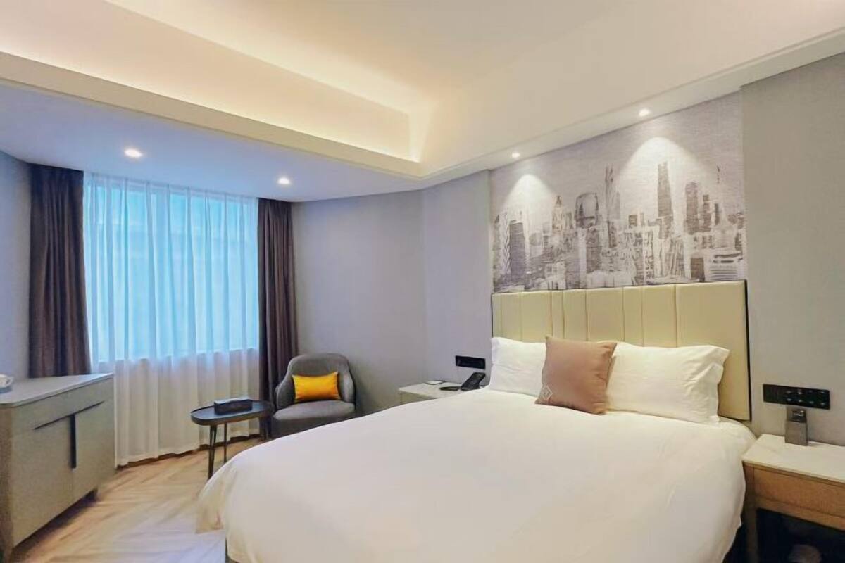 Une chambre d’hôtel avec un grand lit, un bureau, une chaise, une table de chevet et une fresque représentant un paysage urbain sur le mur.