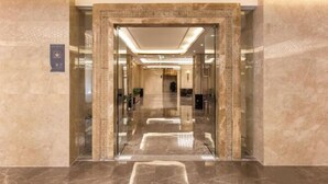 Un lobby moderno de hotel con piso de mármol, puertas de vidrio y ambiente bien iluminado.
