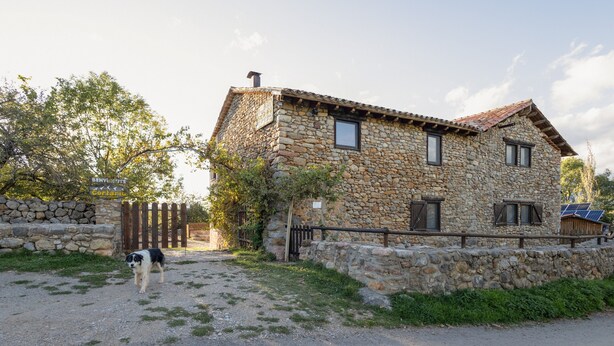 A stone house with a wooden fence, a dog in the foreground, and a clear sky. - Cal Caló – Colònies Cadí is a mountain farmhouse for peaceful groups in Cortariu, La Cerdanya. (Bellver De Cerdanya)