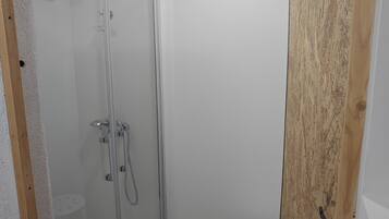 Un baño pequeño y moderno con cabina de ducha de vidrio, un taburete y una puerta de madera.