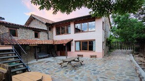 A stone building with a tiled patio, wooden steps, and a picnic table. - Cal Caló – Colònies Cadí is a mountain farmhouse for peaceful groups in Cortariu, La Cerdanya. (Bellver De Cerdanya)