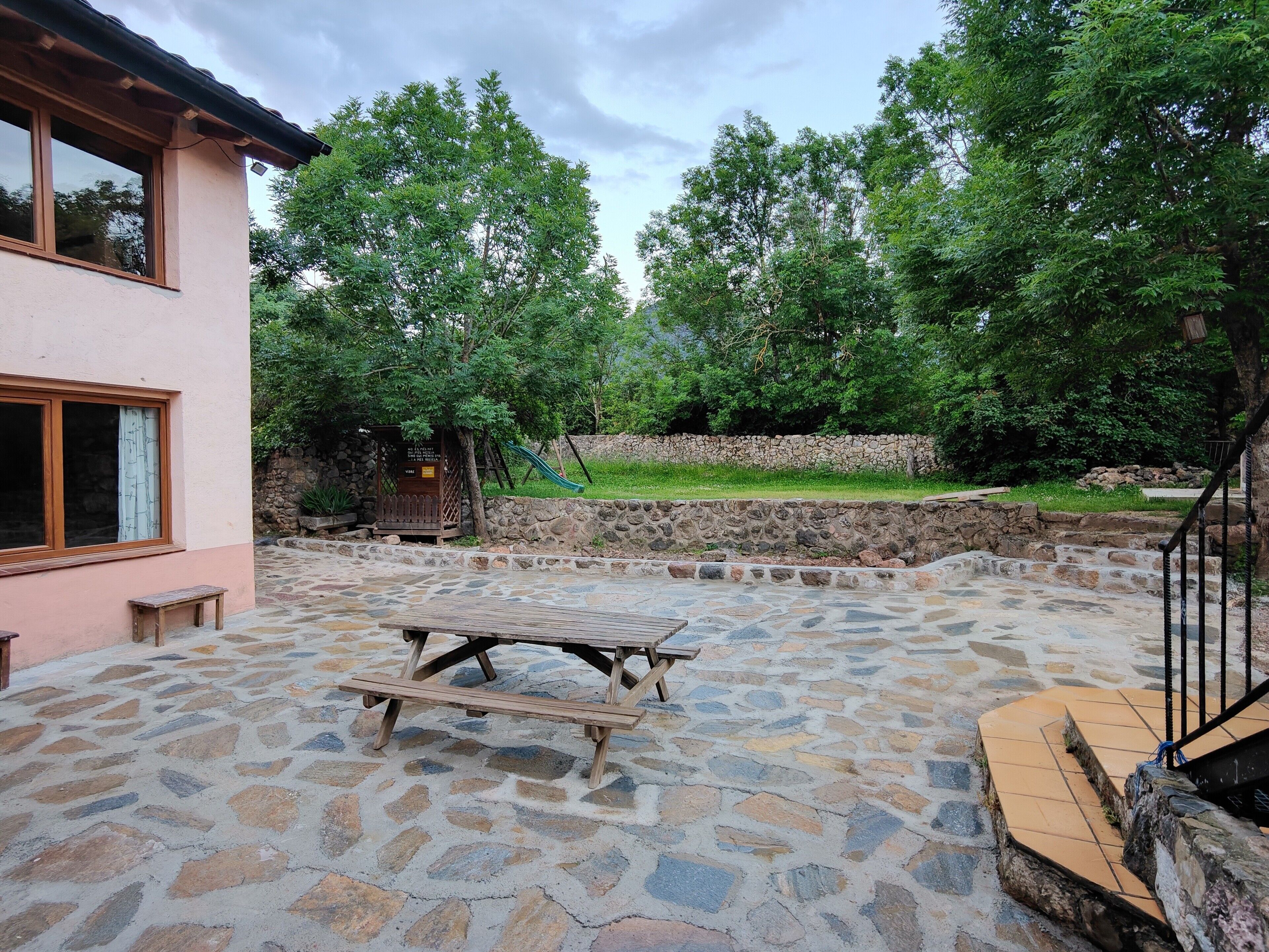 A stone patio with a picnic table, a stone wall, and a playground in the background.