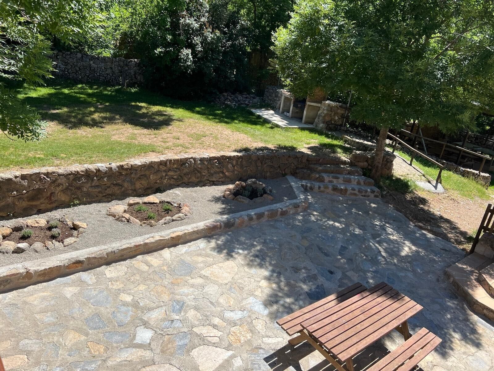 A stone patio with a wooden bench, surrounded by stone walls and greenery.