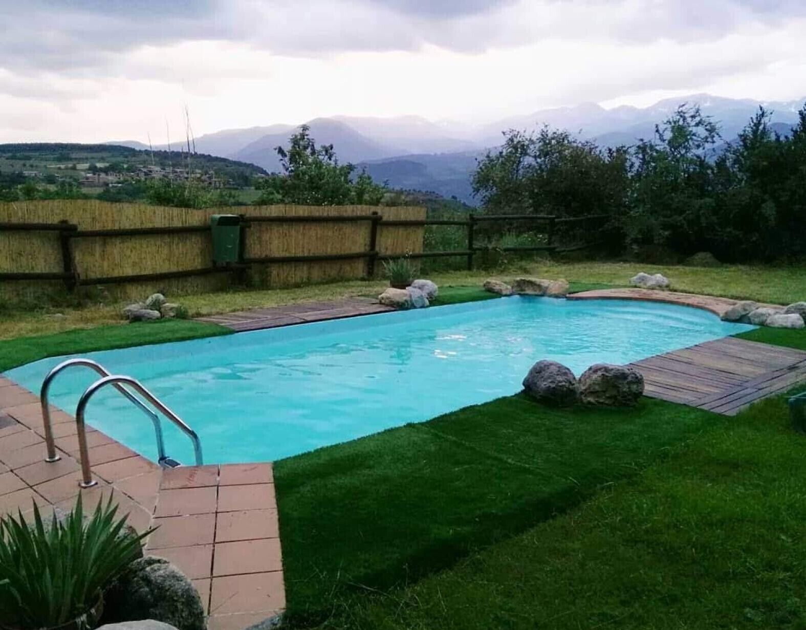 Piscina rectangular con muelle de madera, rodeada de césped y una cerca de madera.