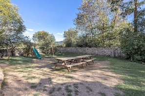 A picnic table set in a grassy area with a stone wall and trees in the background.