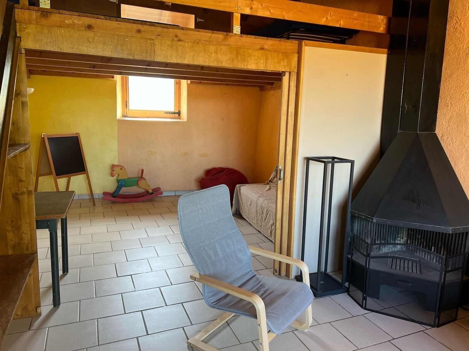 Une pièce avec un plafond en bois, une cheminée, un lit, un cheval à bascule et une chaise.