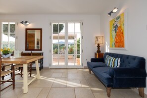 Une pièce comprenant une table à manger, un canapé, un tableau et une vue sur l’extérieur, visible à travers une porte vitrée.