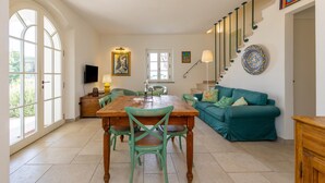 Un vaste espace de vie comprenant une table à manger en bois, un canapé de couleur turquoise et un escalier agrémenté d’une plaque décorative.