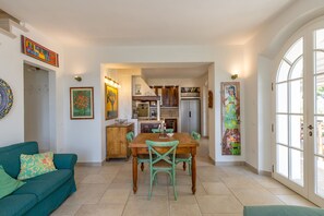 Un comedor con una mesa y sillas de madera, un sofá verde y una cocina al fondo.