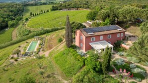 Un bâtiment rouge doté de panneaux solaires, entouré d’une végétation luxuriante et de vignobles.