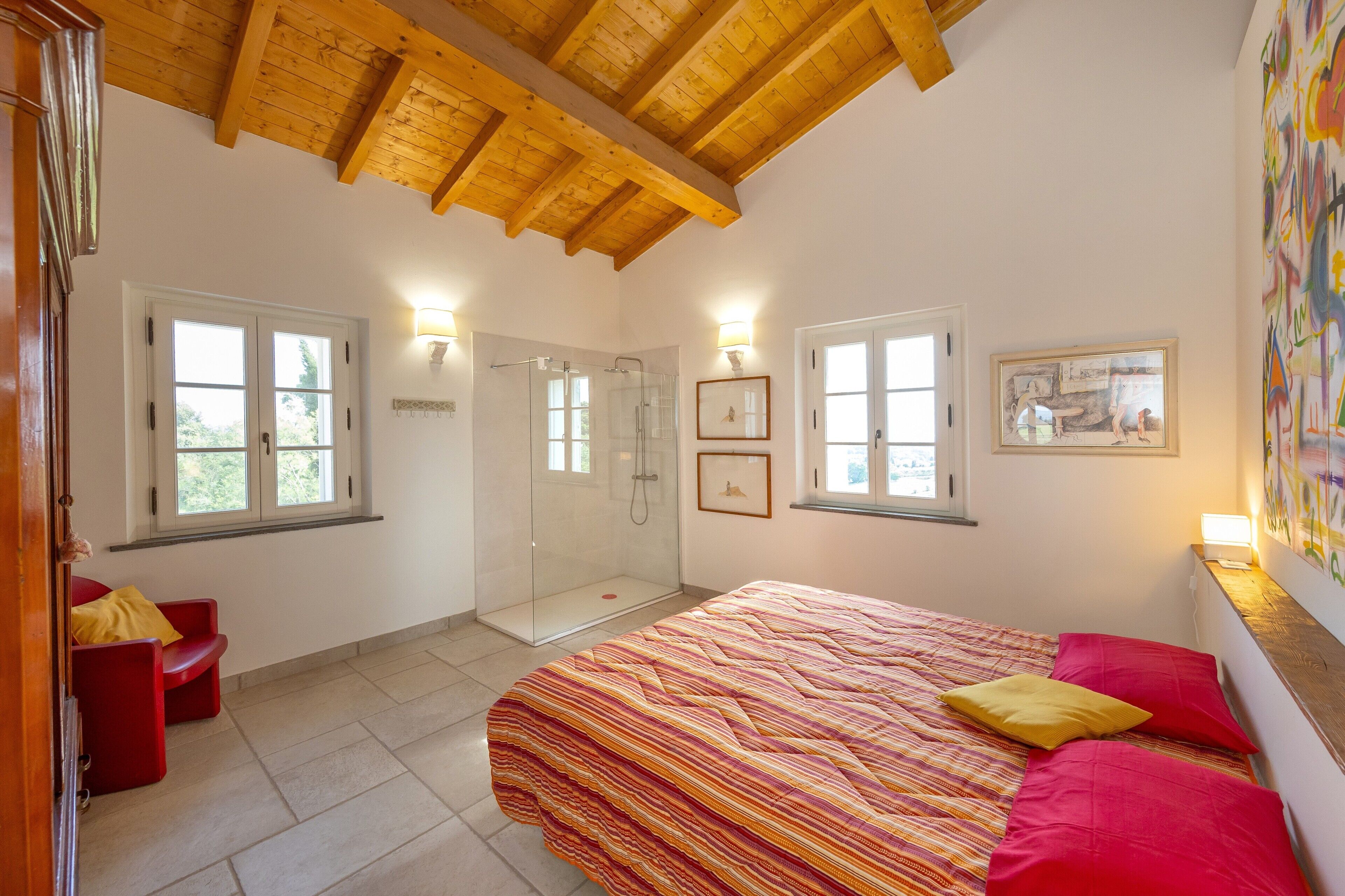 Ein Schlafzimmer mit Bett, roten Kissen, einer Dusche und einer Glastür.