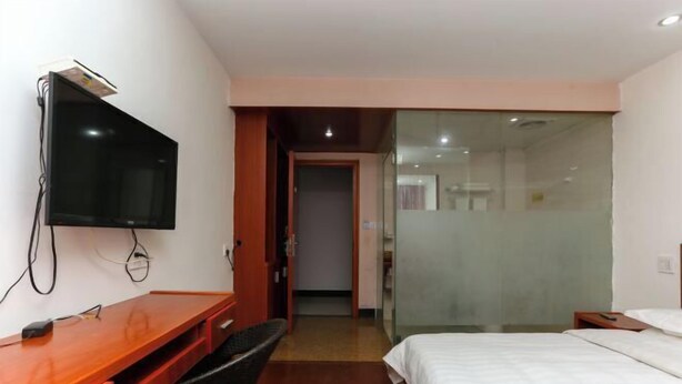 Ein Hotelzimmer mit Schreibtisch aus Holz, Flachbildfernseher, Bett und einer Trennwand aus Glas.